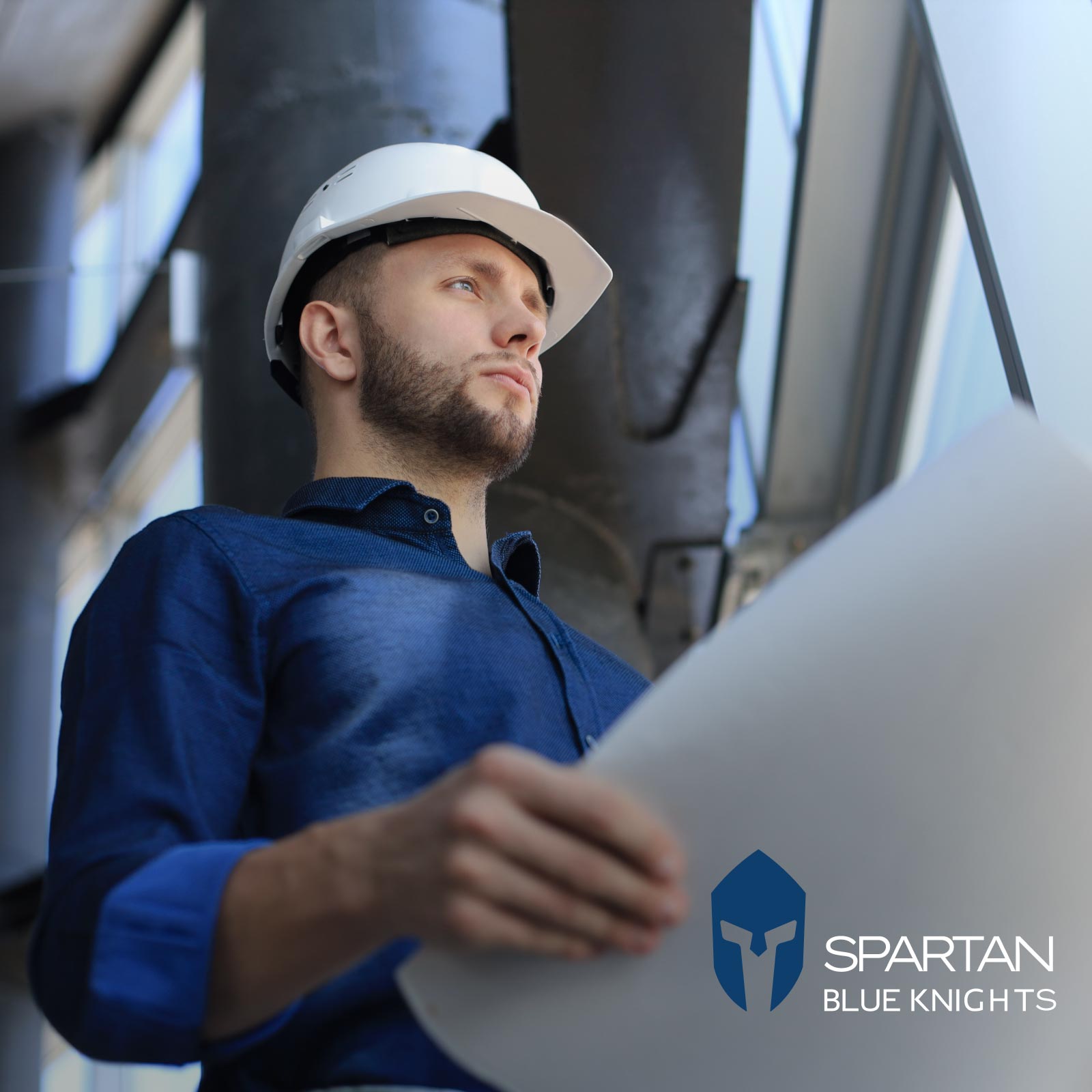 A construction professional wearing a white hard hat and a blue shirt, holding architectural plans.